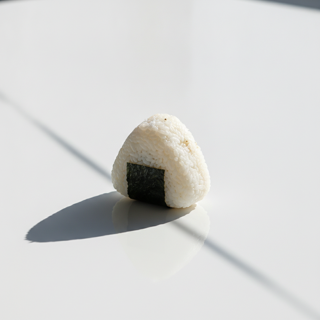 白い無菌質なテーブルの上に置かれた一個のおにぎり。コンビニ食品のデメリットを象徴する、冷たく人工的な雰囲気の写真。